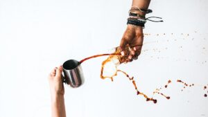 Verschütteter Kaffee aus einer Tasse in einen Becher, dynamische Szene mit spritzender Flüssigkeit.